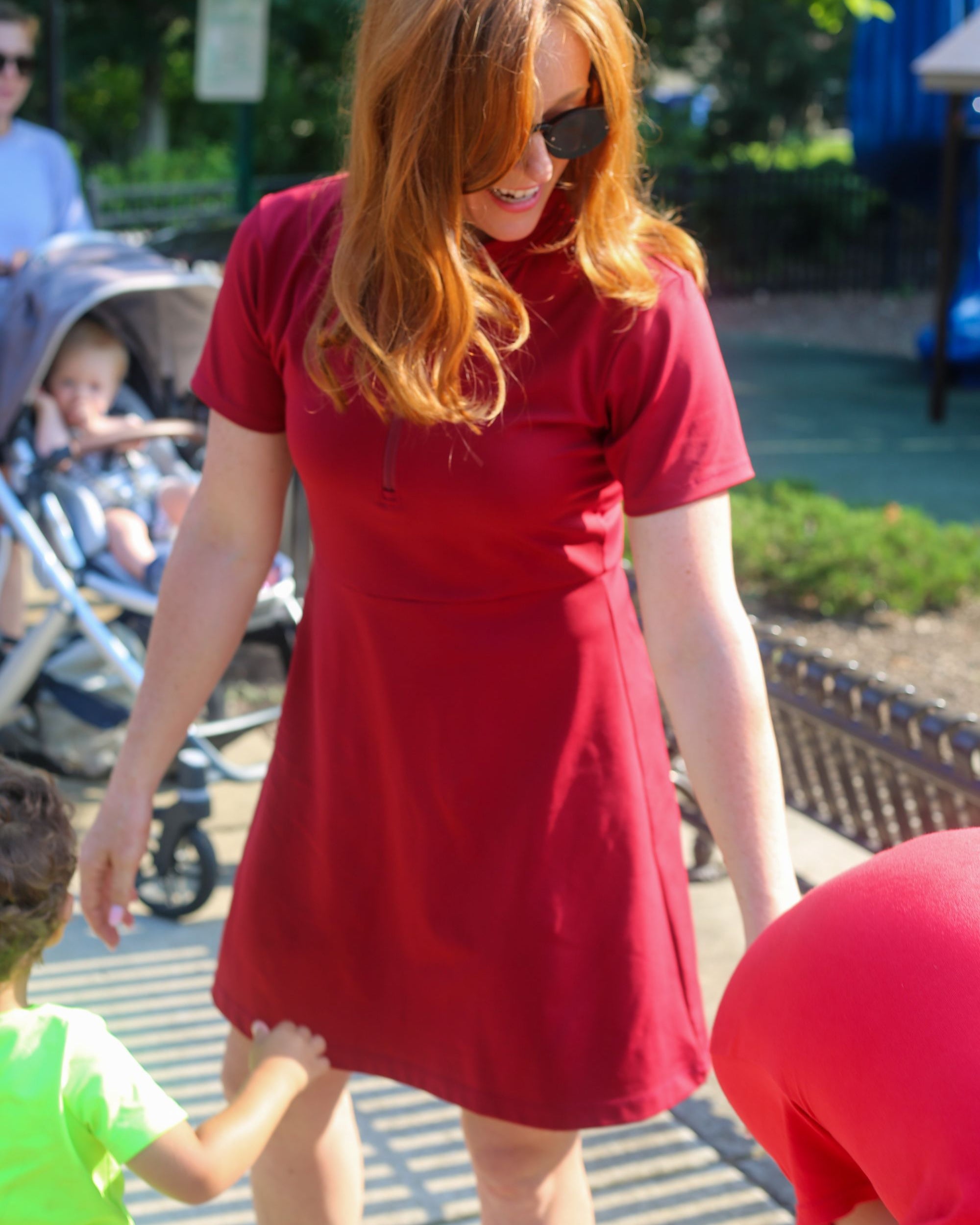 Detail shot of woman wearing red Betty Quarter Zip Dress at the park, featuring the high-quality performance fabrics and UV protection.