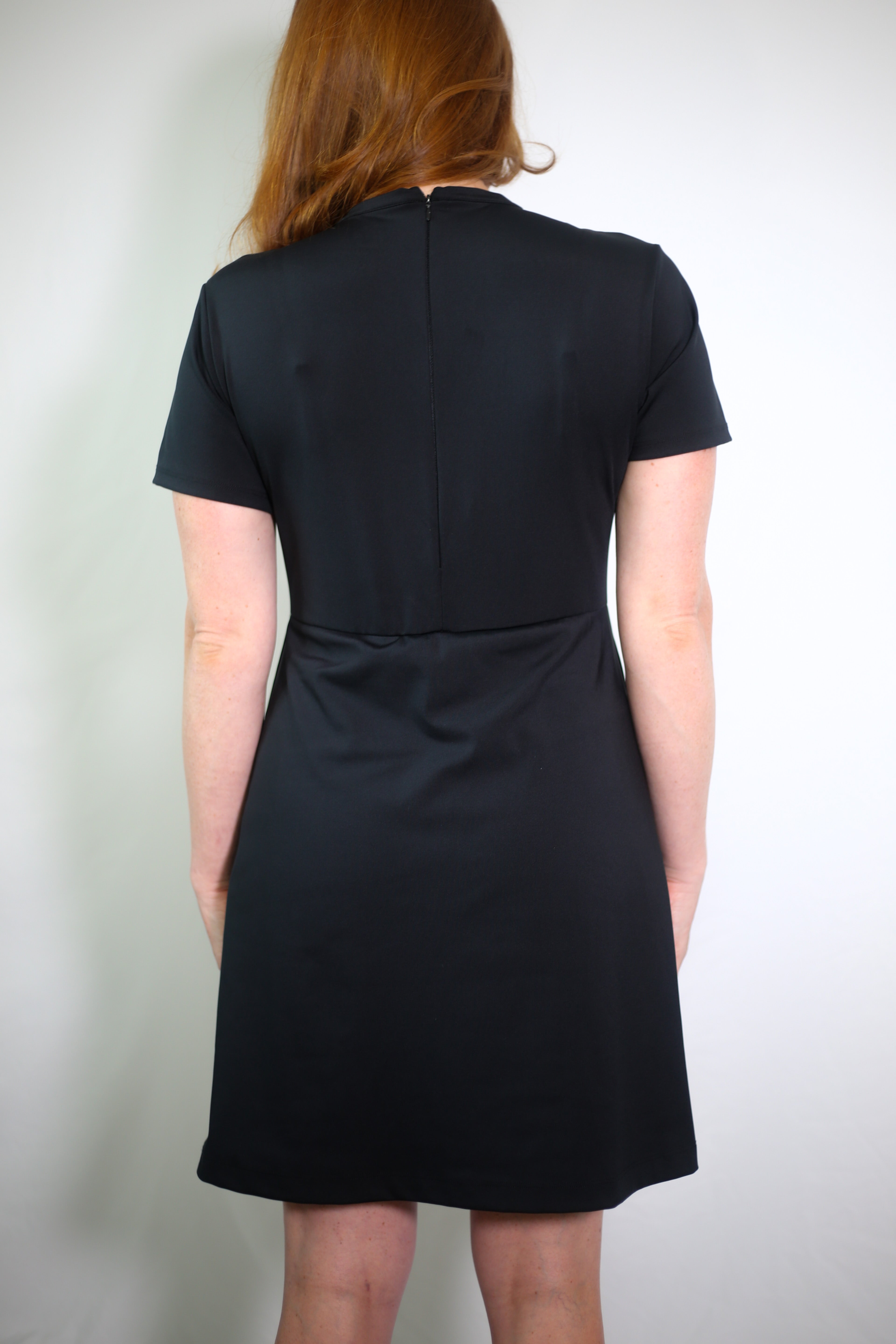 Woman wearing the Ace Henley Dress in black showcasing the back zipper and high-quality performance fabrics.