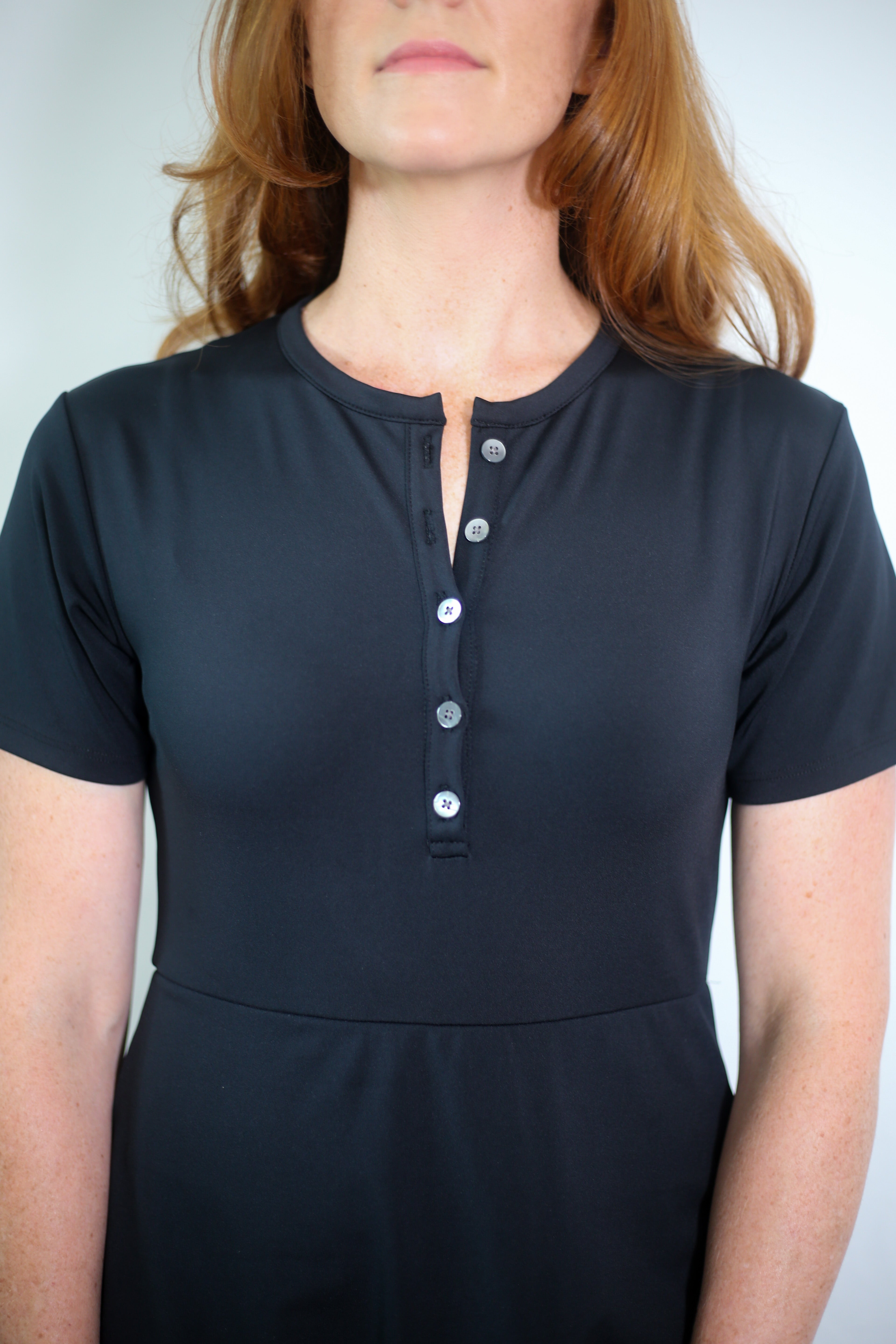 Woman wearing Ace Henley dress in black with detail shot of high-quality performance fabrics.