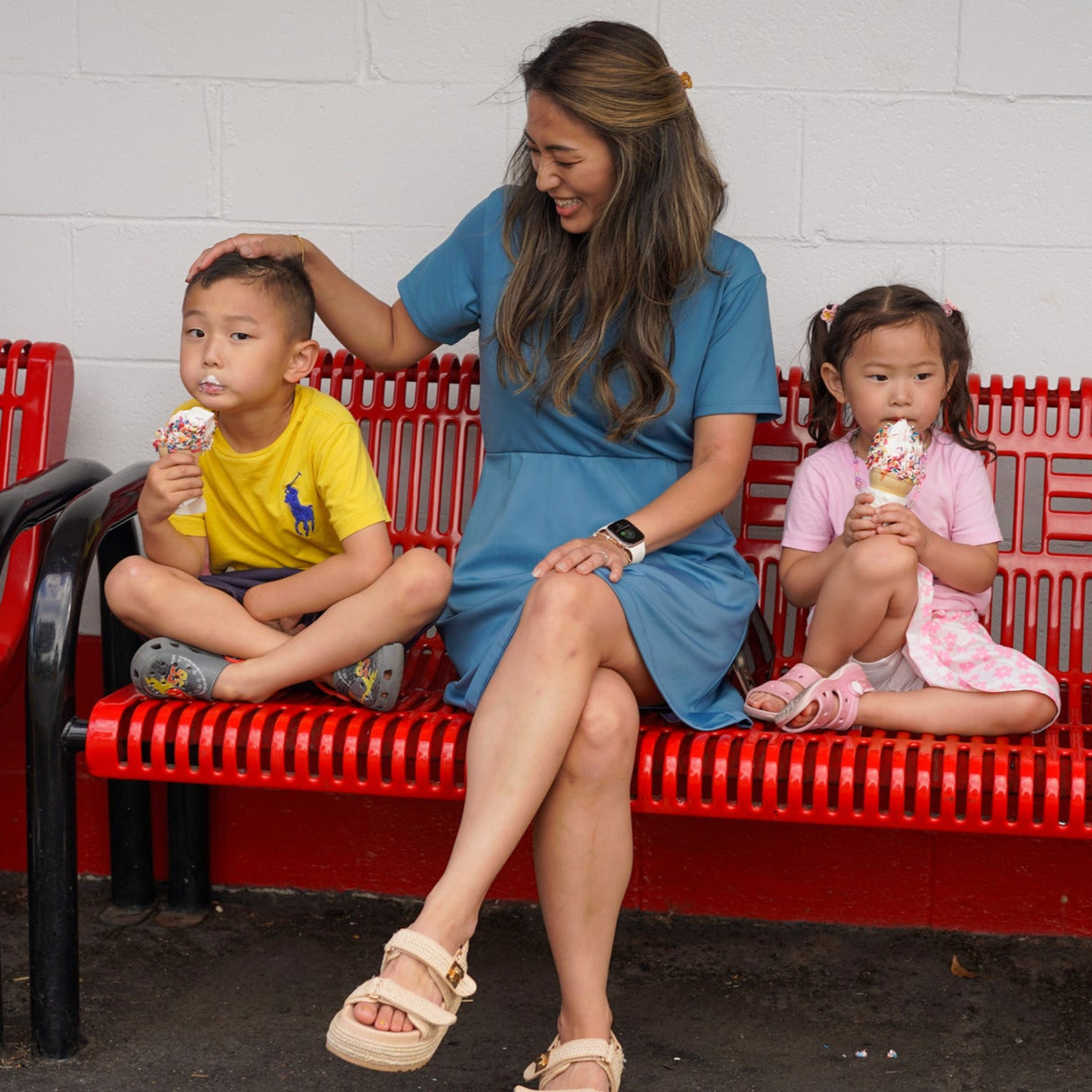 Mother wearing Clarece Polo dress in light blue while enjoying ice cream with her son and daughter at the park. Dress is styled with beige platform sandals, smart watch, and gold bracelet.