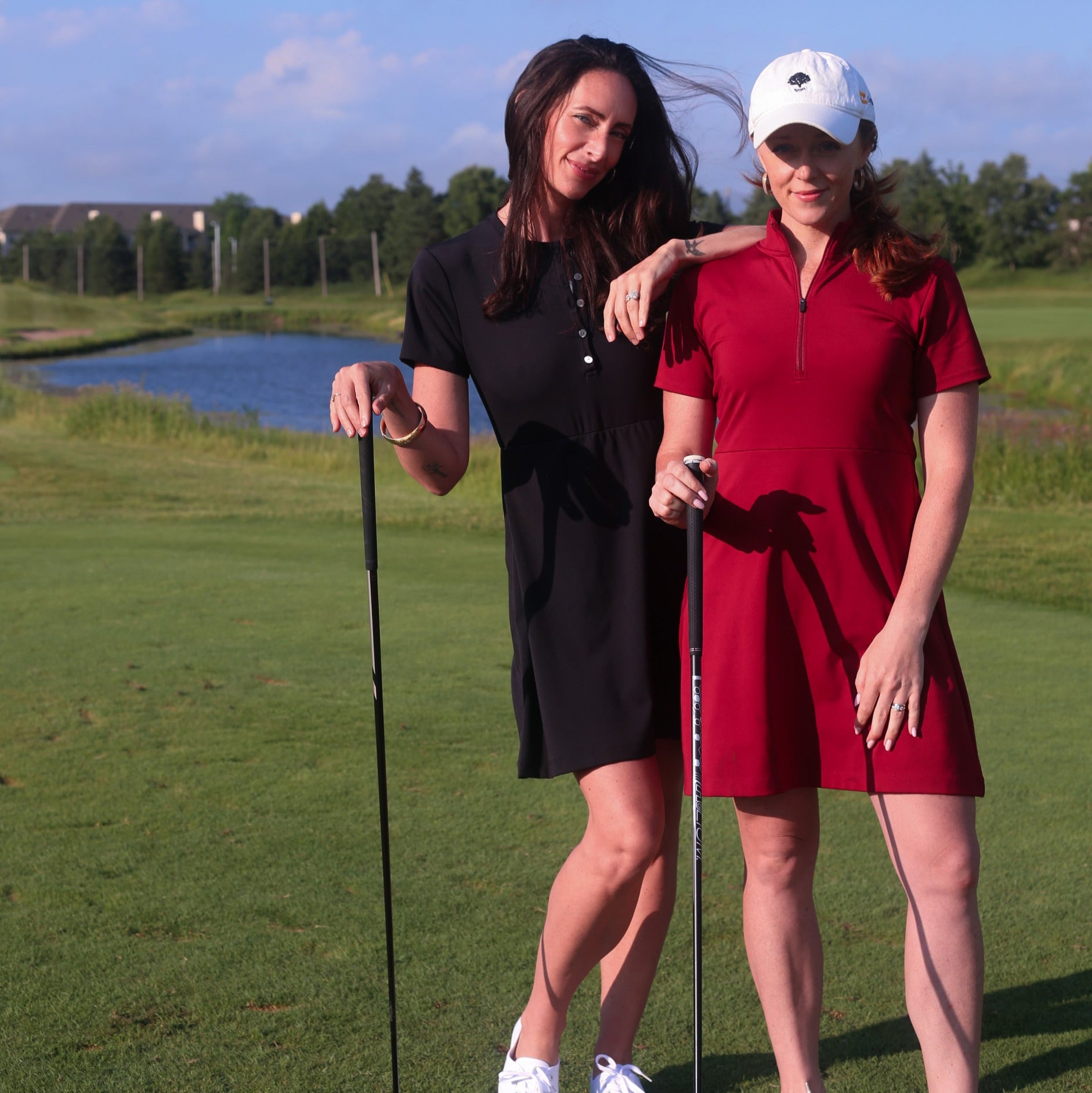 Two women golfing in the black Ace Henley Dress and red Betty Quarter Zip dress showcasing their high-quality performance fabrics, moisture-wicking, and UV protection.