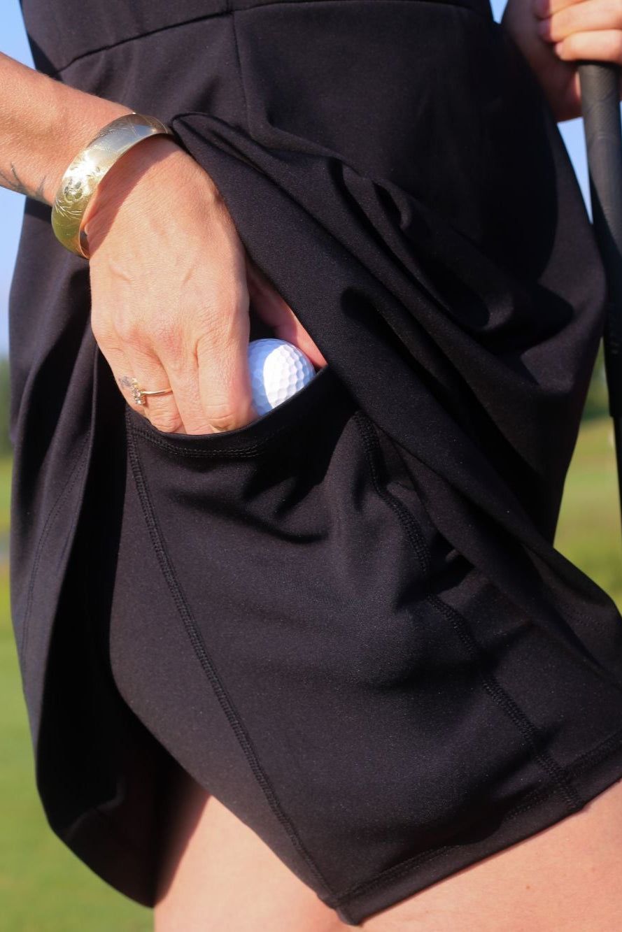 Person holding a golf club and putting a golf ball into their built-in dress shorts on a golf course with a blurred background