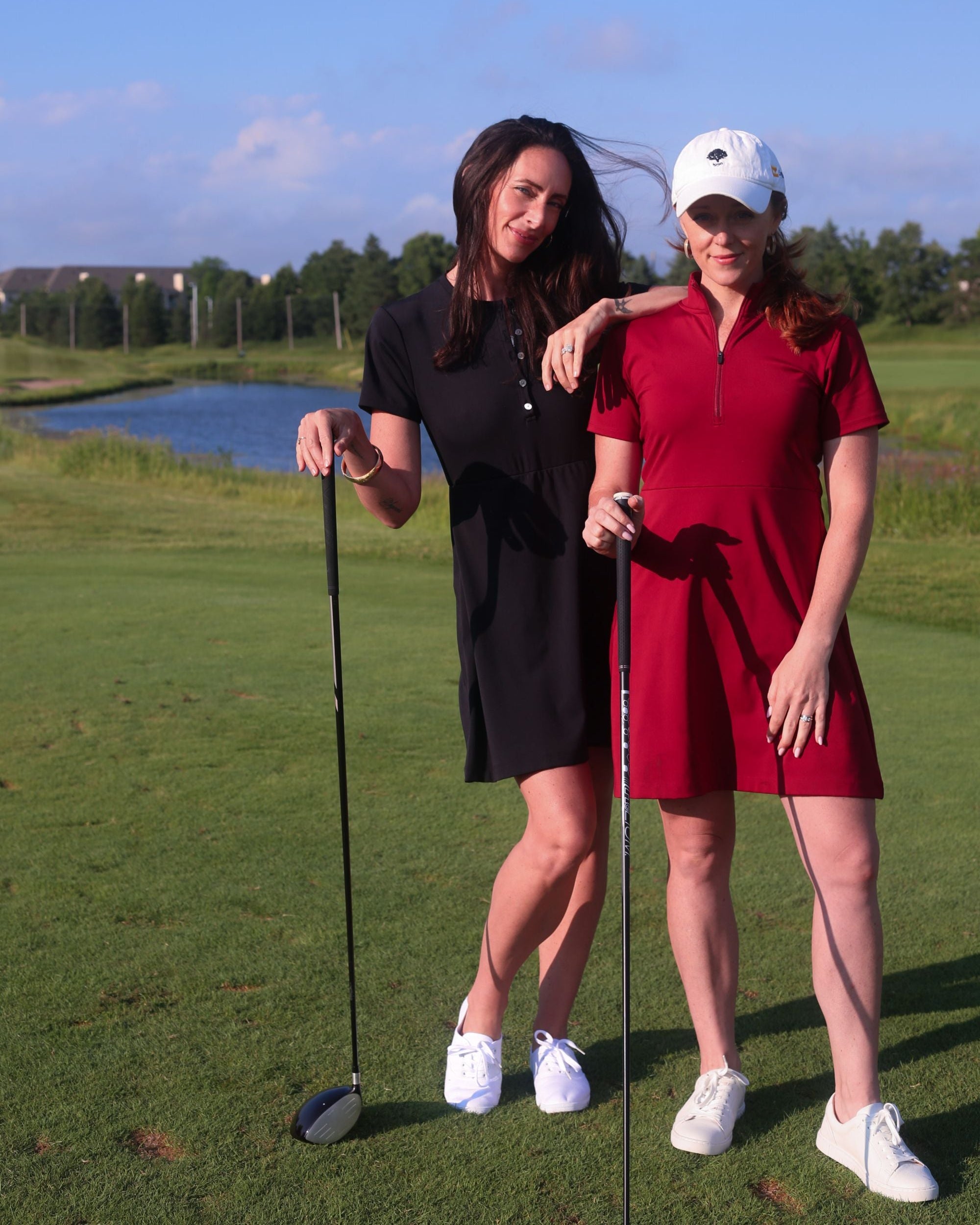 Two women golfing in the black Ace Henley Dress and red Betty Quarter Zip dress showcasing their high-quality performance fabrics, moisture-wicking, and UV protection.