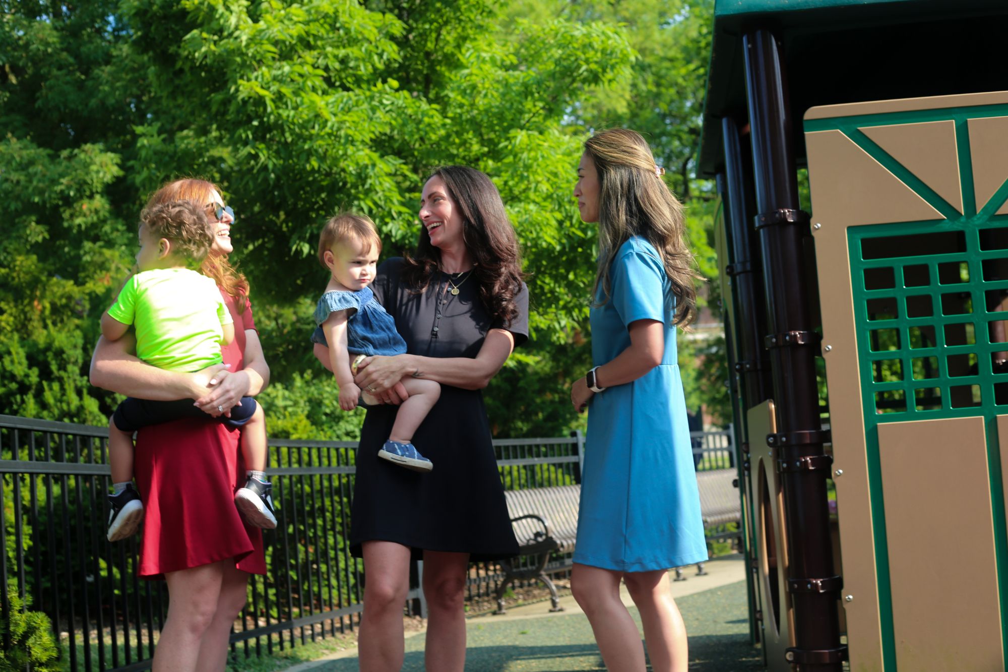Three mothers are the park wearing Nicole Clarece dresses. One woman wears the Betty Quarter Zip Dress in red, one wears the Ace Henley Dress in black and the third wears the Clarce Polo Dress in light blue.