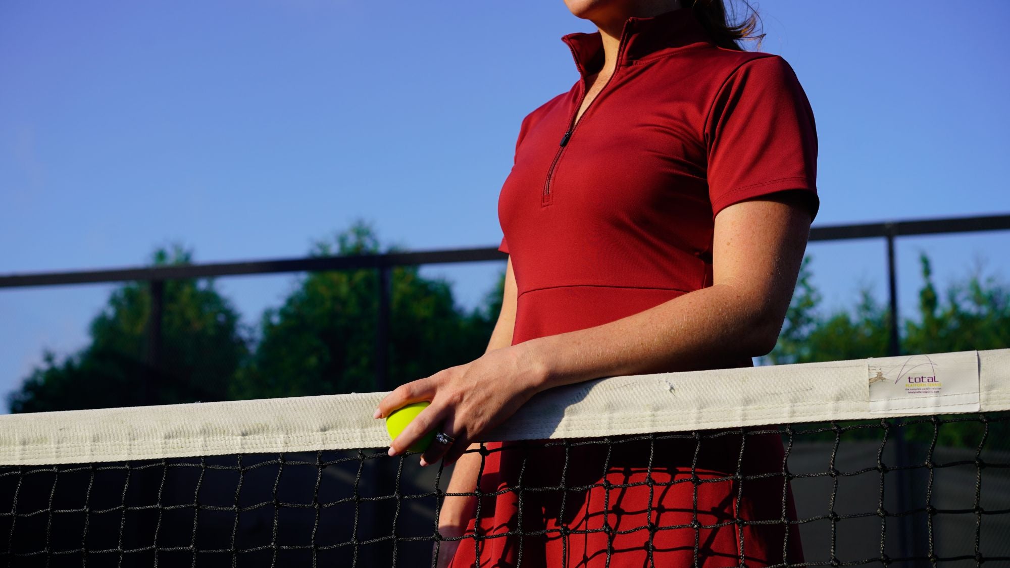 Detail shot of woman wearing red Betty Quarter Zip Dress at the tennis court, featuring the high-quality performance fabrics and functional zipper in the neckline.