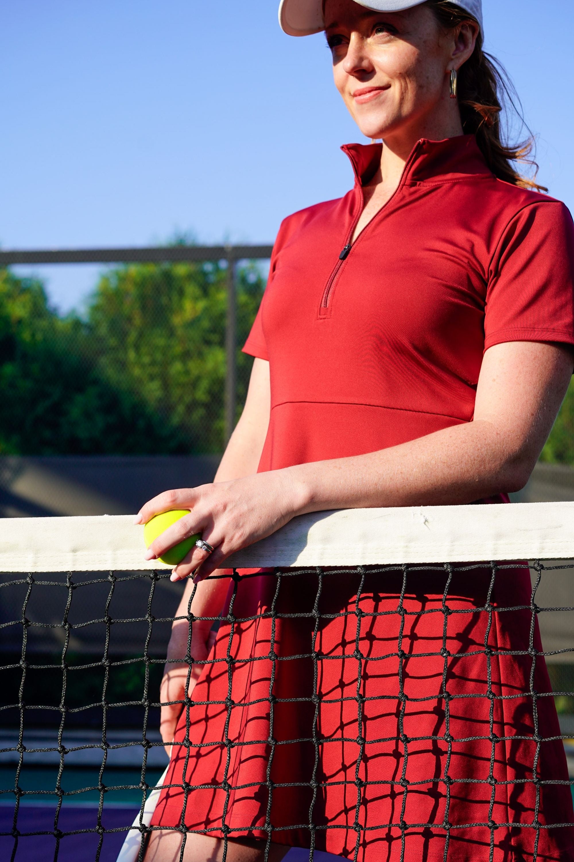 Detail shot of woman wearing red Betty Quarter Zip Dress at the tennis court, featuring the high-quality performance fabrics and functional zipper in the neckline.