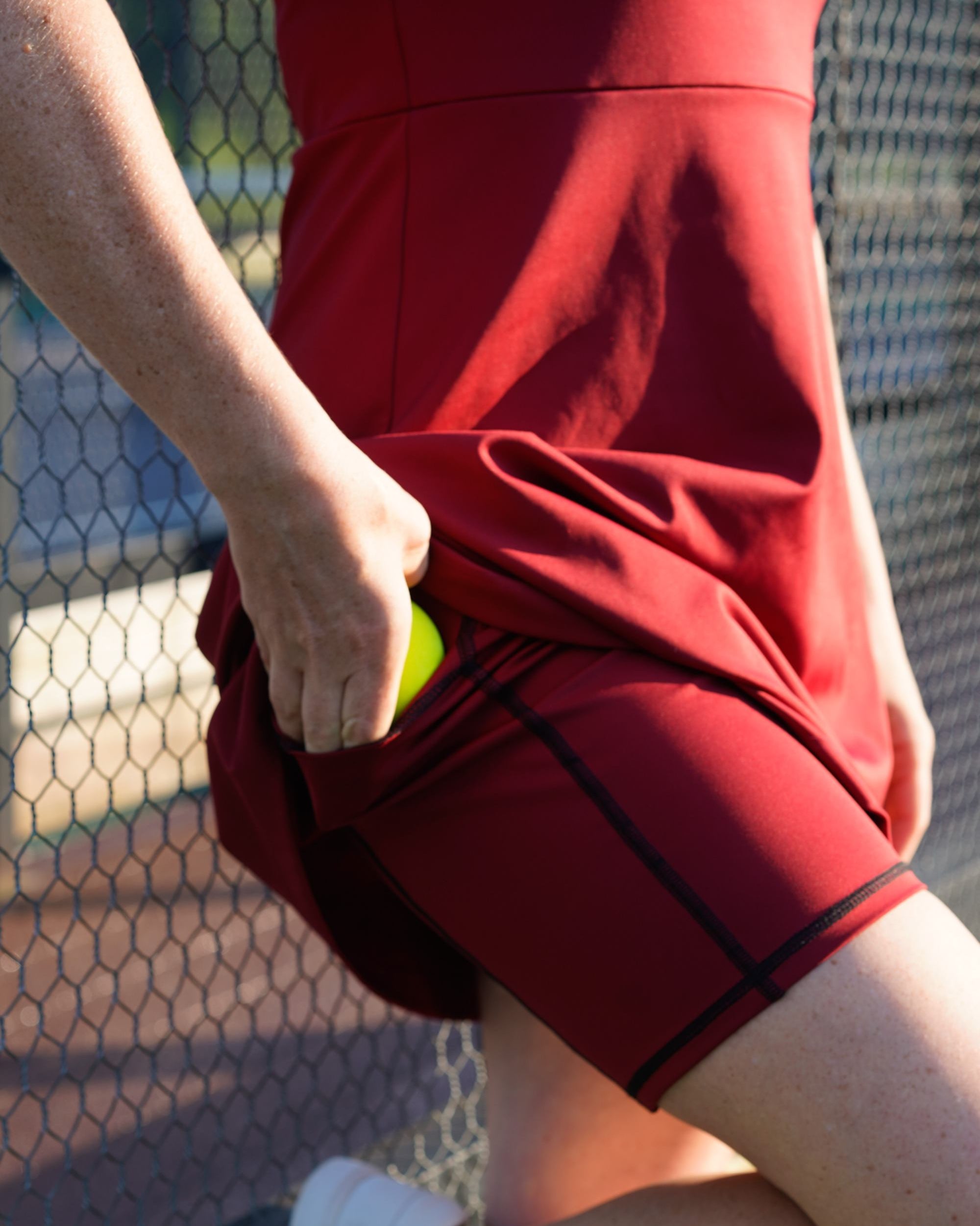 Detail shot of woman wearing red Betty Quarter Zip Dress at the tennis court, featuring the high-quality performance fabrics and versatile, stretchy pockets of the matching detached short.