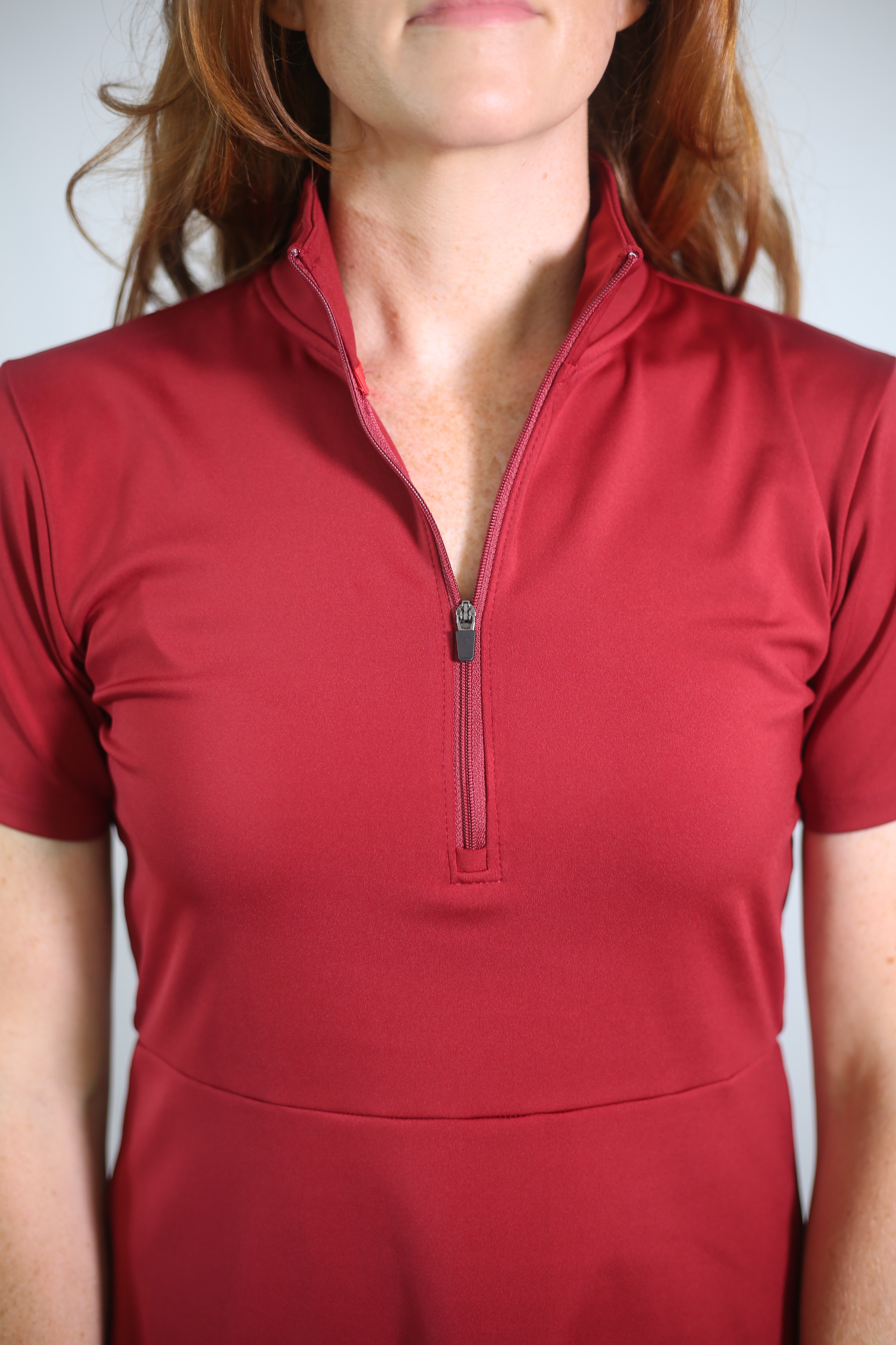 Detail shot of woman wearing Betty Quarter Zip dress in red showcasing the functional zipper. This dress is made from recycled performance fabrics and offers 4-way stretch, UV protection, and moisture-wicking for versatility, comfort and flexibility. 